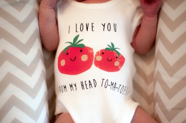 Meal Delivery Services That Will Make Parent Life Easier, a baby wearing a white onesie with two tomatoes with cute faces on them and the punny phrase ' I love you from my head to-ma-toes.'